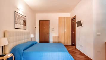 Een hotelkamer met een bed, nachtkastje met lamp, een lijst met afbeelding aan de muur, een garderobe en een televisie.