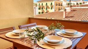 A wooden table set with plates, glasses, and olive branches on a balcony with a view of terracotta-roofed buildings. - (20/30 sq m): living room with kitchenette, double bed, single folding bed, bathroom. <br>Features: <br>tv, <br>ironing board and iron (on request) <br>kitchenette with induction hub, <br>oven, <br>kettle, <br>microwave <br>safe, <br>1 beach umbrella, <b (Santa Teresa di Gallura)