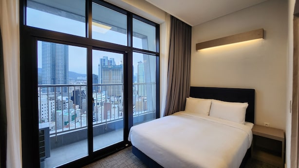 A hotel room with a large window offering a city view, a neatly made bed, and a modern headboard. - Haeundae Blue Story Hotel (Busan)