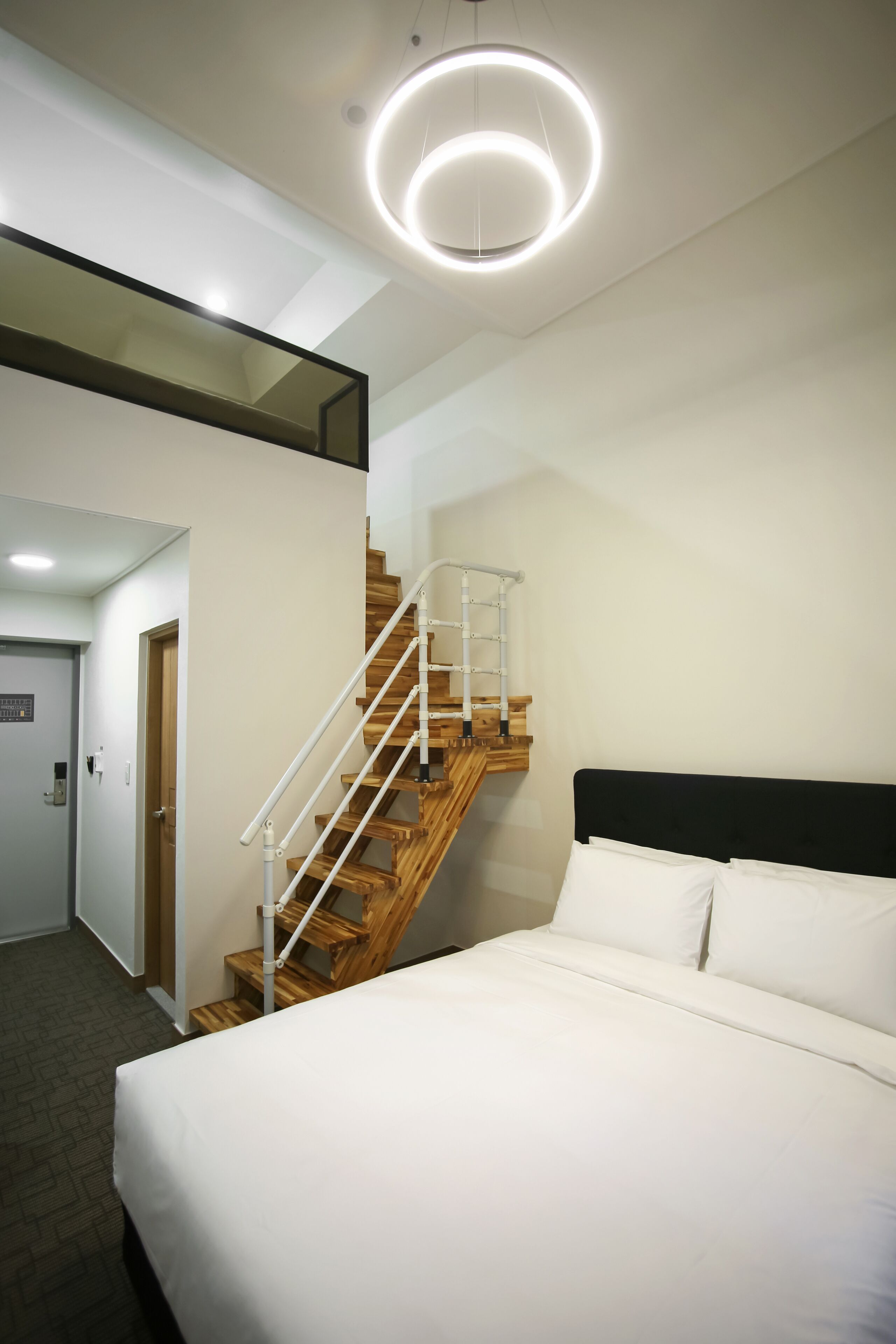 A modern hotel room with a large bed, a wooden staircase, and a circular light fixture.