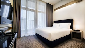 A hotel room with a large bed, a TV on a stand, a desk with a lamp, and a view of the outdoors through sheer curtains. - Haeundae Blue Story Hotel (Busan)