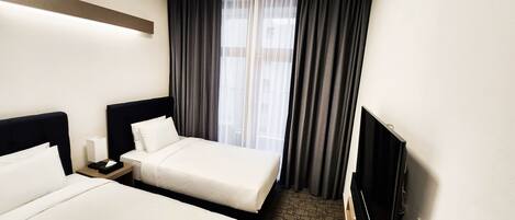 A hotel room with two beds, a nightstand, a TV, and a window with curtains.