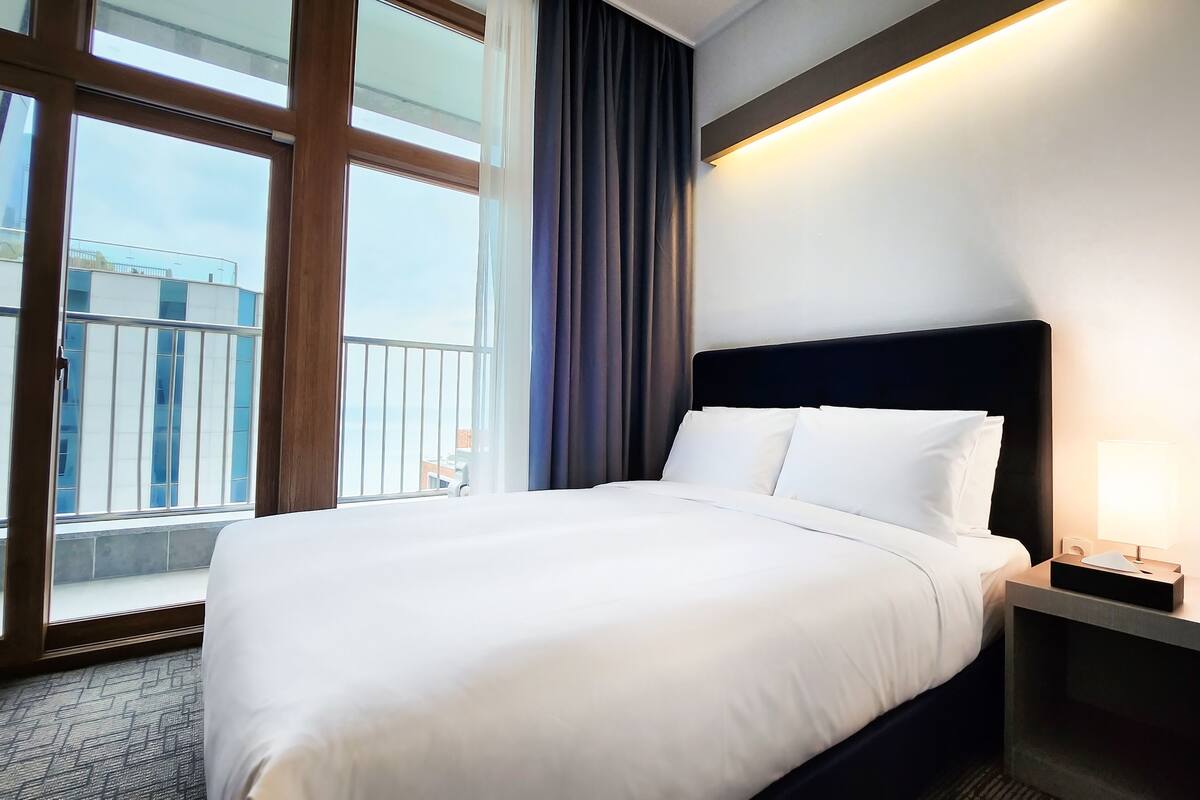 Ein Hotelzimmer mit einem großen Bett, einem Nachttisch mit Lampe, Blick auf den Balkon und einem modernen Design.
