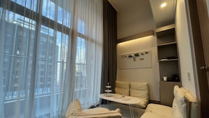 A modern hotel room with a large window, a sofa, a small table, and a wall-mounted board. - Haeundae Blue Story Hotel (Busan)