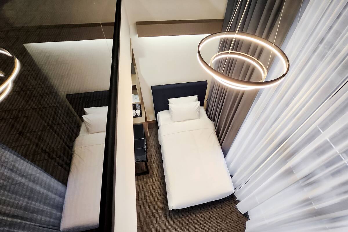 Ein Hotelzimmer mit einem Bett, einem Schreibtisch und einem Stuhl. Es gibt ein Fenster mit Vorhängen und eine Deckenleuchte.