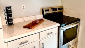 A compact kitchen with a stove, oven, white cabinets, and a coffee station.