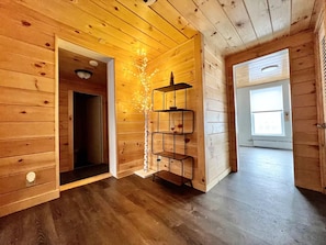 Un intérieur en bois agrémenté d’une étagère métallique à plusieurs niveaux, une porte donnant sur une autre pièce et une fenêtre laissant entrer la lumière naturelle.