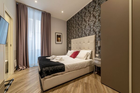 A bedroom with a bed, a bedside table, a TV, and a window with curtains.