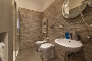 A bathroom with a shower, two toilets, a sink, and a mirror.
