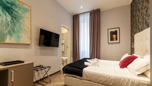 Ein Hotelzimmer mit Bett, Fernseher, Schreibtisch und einem Fenster mit Vorhängen.