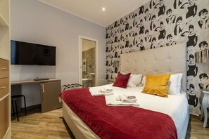 A bedroom with a bed, a TV, a desk, and a bathroom visible through an open door.