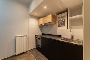 A compact kitchen with a built-in oven, a stainless steel sink, and a wooden cabinet above the stove.