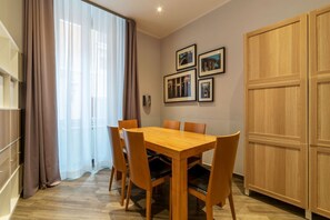Un coin repas avec une table et des chaises en bois, une grande fenêtre avec des rideaux et des tableaux encadrés accrochés au mur.