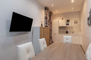 A modern kitchen with white cabinets, a microwave, and a coffee maker. There is a dining table with white chairs.