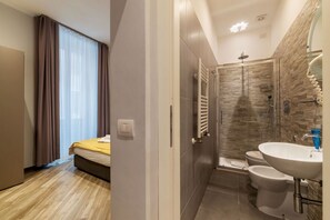 A modern hotel room with a bed, a bathroom with a shower, and a sink.