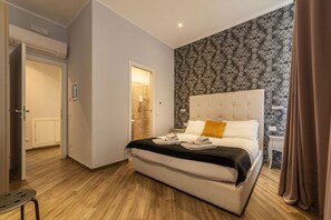 A bedroom with a large bed, a bedside table, a nightstand, a door leading to a bathroom, and a patterned wallpaper.