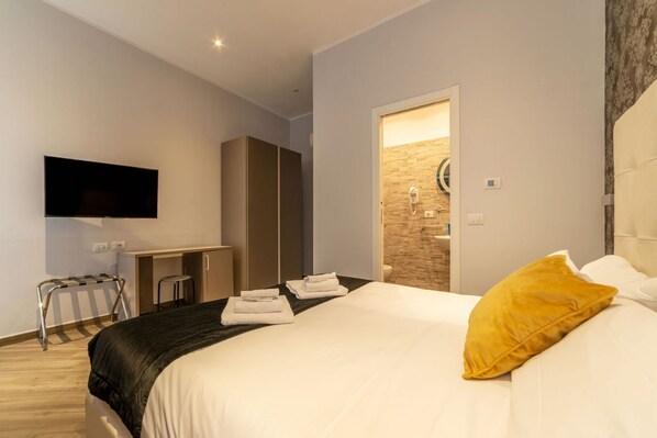 A modern hotel room with a bed, a desk, a television, and a bathroom visible through an open door.