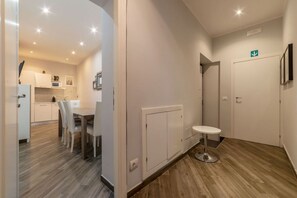 A modern hotel room with a wooden floor, a dining area with a table and chairs, a small round table, and a white wall with a door. - Frattina 2 - FromHometoRome (Roma)