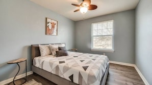 A bedroom with a bed, a ceiling fan, a window, and a small table. - Spacious Farmhouse  Townhome*Walk to AT&T Stadium* (Arlington)