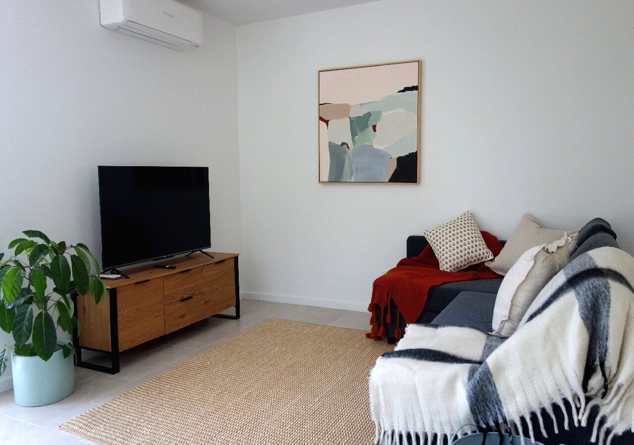Un salon moderne avec un téléviseur à écran plat posé sur un meuble en bois, une grande peinture abstraite accrochée au mur, un canapé confortable agrémenté d’un plaid et une plante en pot.