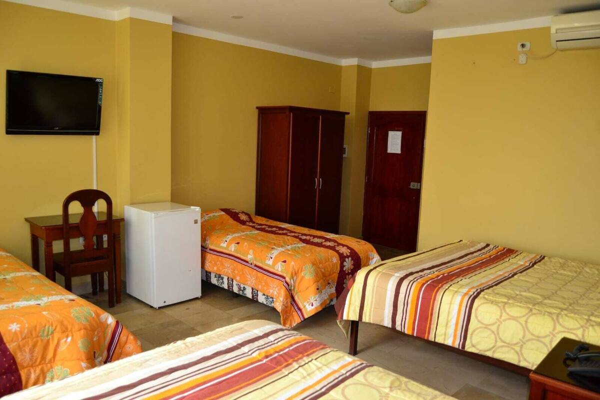 A room with two beds, a small table, a chair, a television, and a wardrobe.