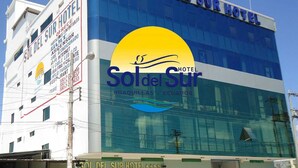 Un edificio de hotel con un gran logotipo amarillo y azul, múltiples ventanas y un letrero que indica que está ubicado en Hualqui, Ecuador.