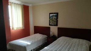 Una habitación de hotel con dos camas individuales, una mesita de noche, una lámpara y un cuadro en la pared.