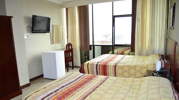Habitación de hotel con dos camas, televisión, refrigerador y ventana con cortinas.