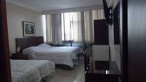 Habitación de hotel con dos camas, televisión, escritorio y ventana con cortinas.