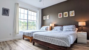 A bedroom with two beds, a ceiling fan, a window with curtains, and framed artwork on the wall.