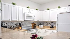 A modern kitchen with white cabinets, a granite countertop, a stainless steel stove, a microwave, a toaster, and a blender.