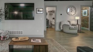 A modern living room with a large flat-screen TV, a round clock, and a comfortable seating area. - The 418 ~ An 1866 Build with Modern Comforts (Fort Wayne)