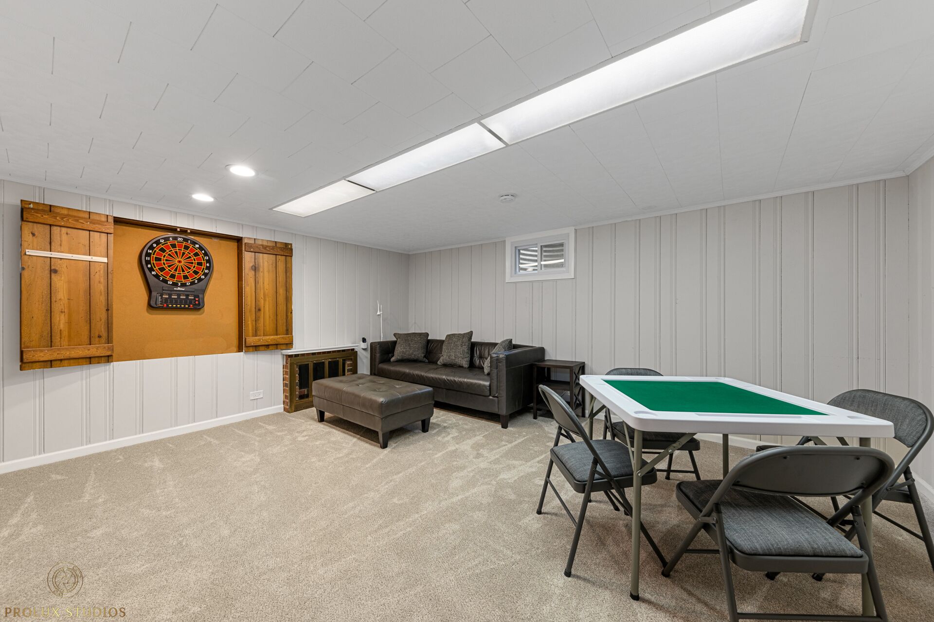 A room with a pool table, a leather sofa, a dartboard, and a small window.