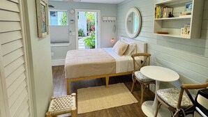 Un dormitorio con cama, una mesita redonda pequeña, dos sillas, una estantería, un espejo y vistas al exterior.