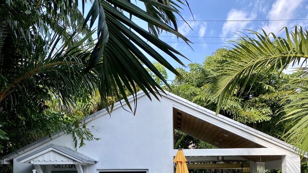 Una casa moderna con fachada blanca, un porche cubierto con mobiliario exterior y una variedad de plantas en macetas.