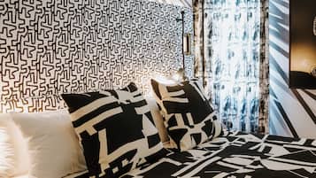 Camera da letto moderna con copriletto a motivi geometrici, testata a fantasia e una grande finestra con tende.