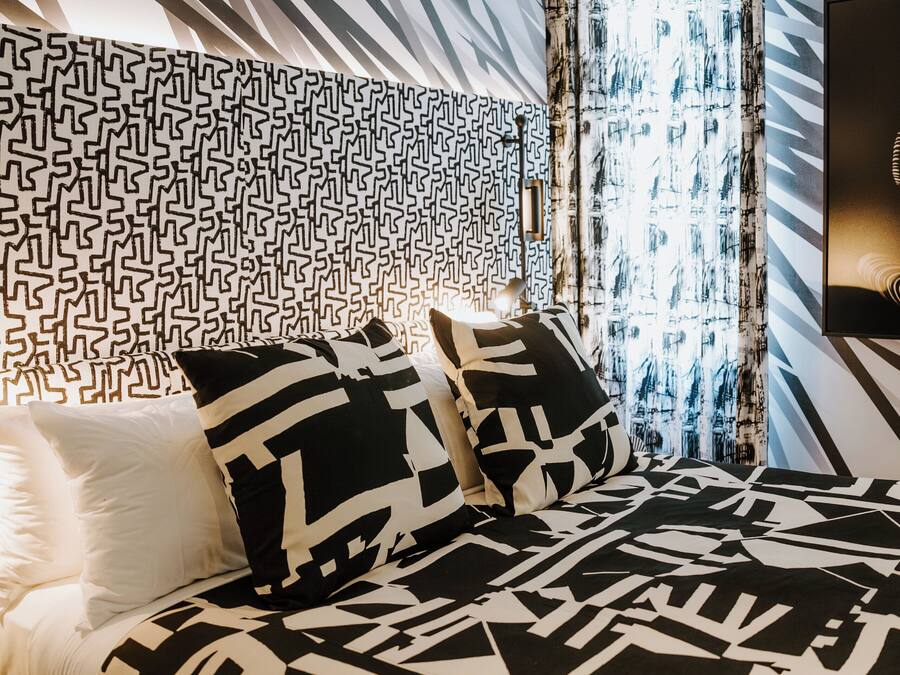Camera da letto moderna con copriletto a motivi geometrici, testata a fantasia e una grande finestra con tende.
