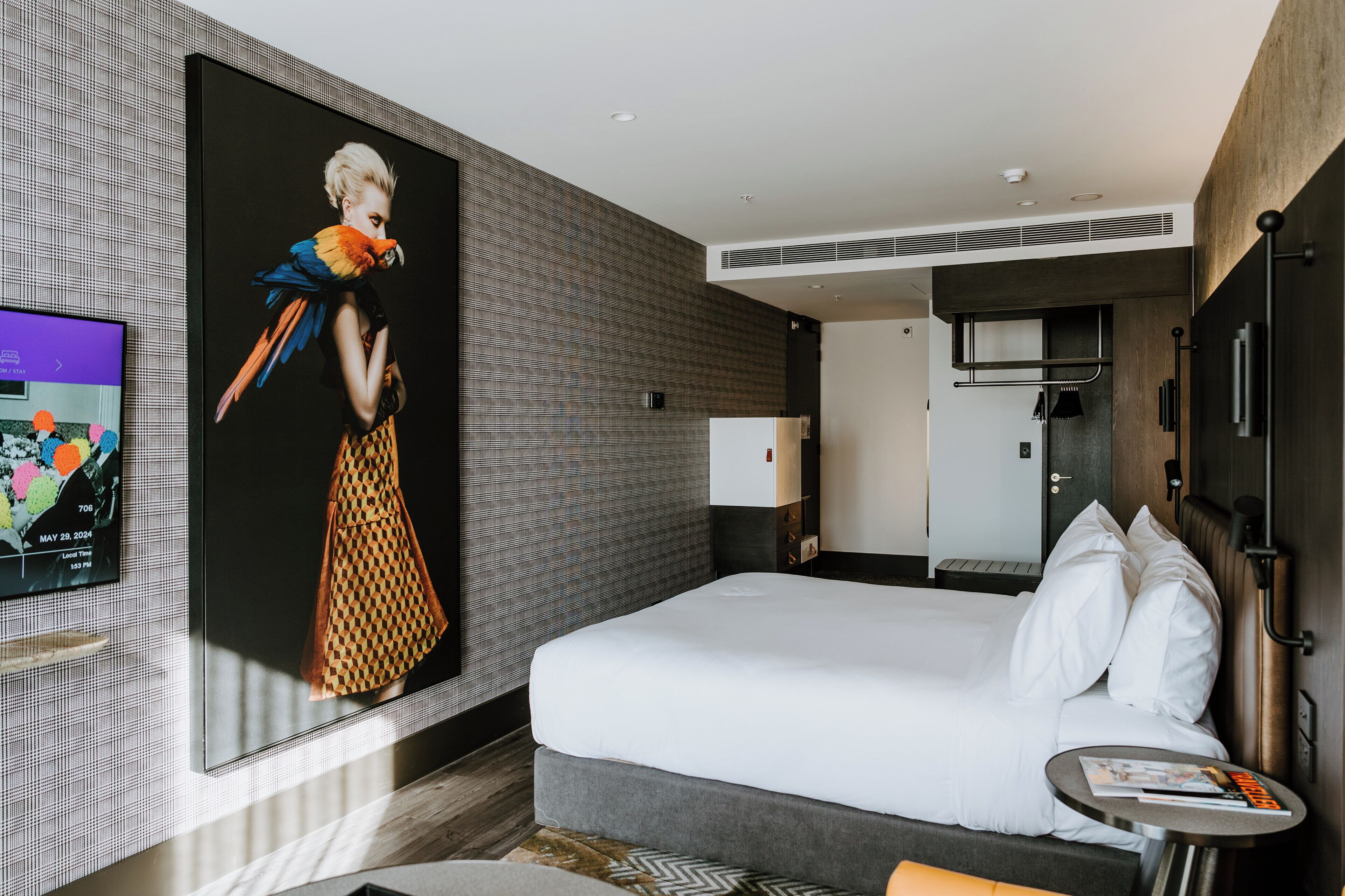 A modern hotel room with a large bed, a small bedside table, a flat-screen TV, and a large poster on the wall.