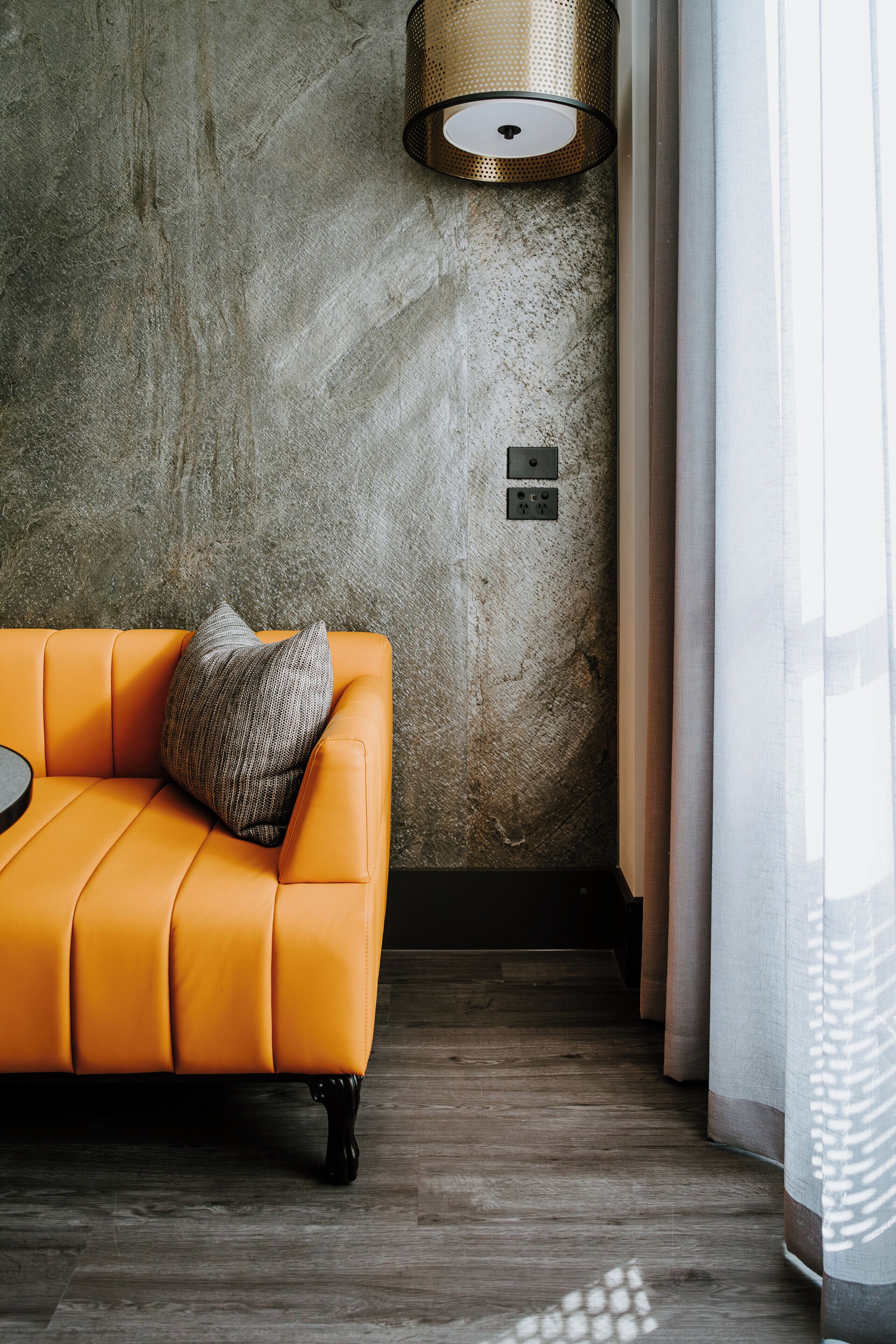 A modern living room with a leather sofa, a textured wall, a floor lamp, and a window with curtains.
