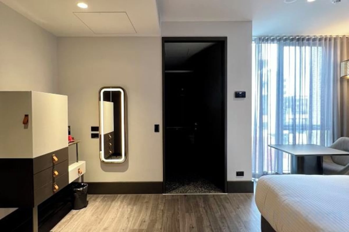 Una habitación de hotel con una cama, un escritorio, un espejo y una puerta que da a otra habitación.