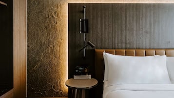 A modern hotel room with a wooden headboard, a bedside table with a clock, and a textured wall.