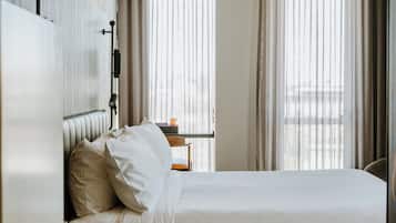 A modern hotel room with a large bed, a bedside table, a lamp, and a view of the city through the window.