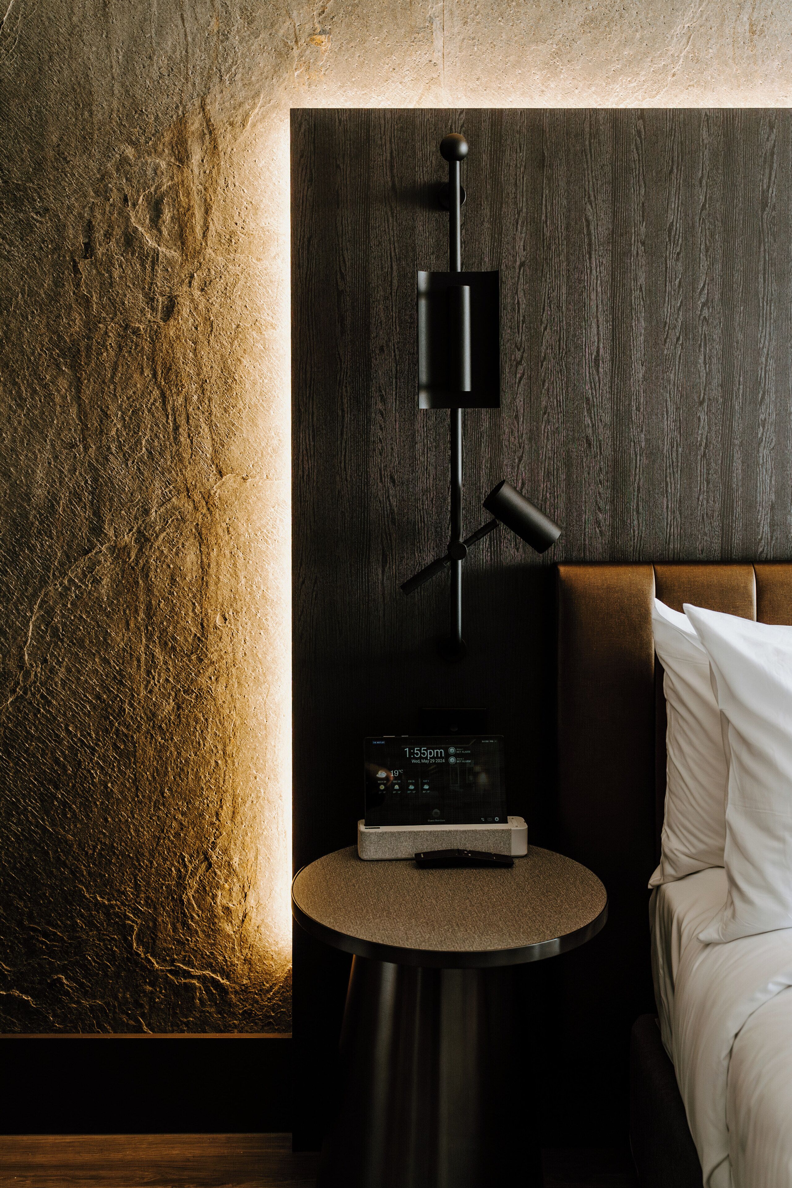 Une chambre d’hôtel moderne avec une tête de lit en bois, une petite table ronde avec une radio et un mur à motifs.