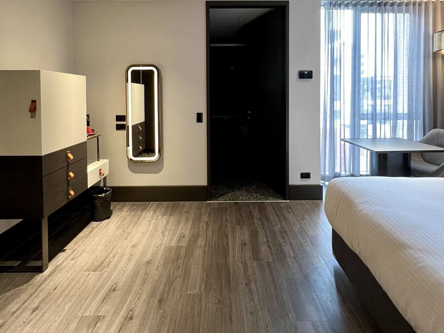 A hotel room with a bed, a dresser, a mirror, and a door leading to a hallway.