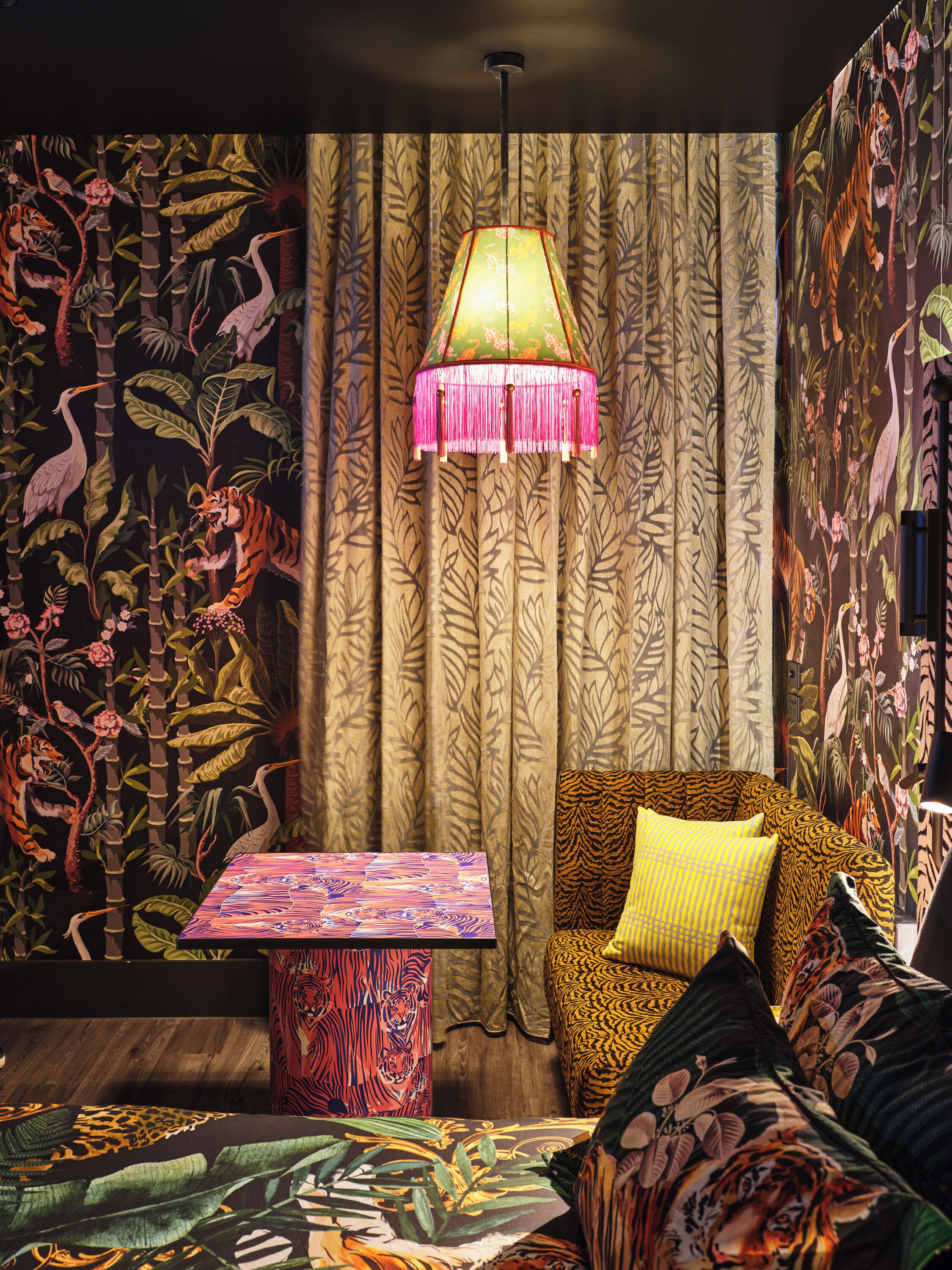 A room with a patterned wall, a hanging lamp, a small table, and a sofa with patterned cushions.