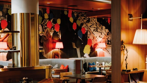 A hotel lobby with leather chairs, a bar area, and a patterned wall. - The Motley Hotel Melbourne, Tapestry Collection by Hilton (Richmond)