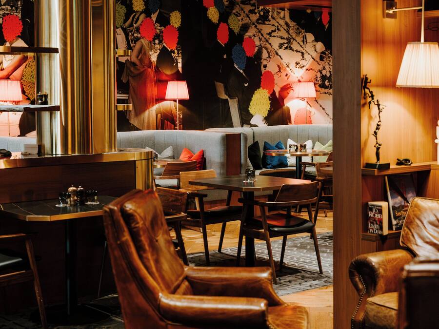 A hotel lobby with leather chairs, a bar area, and a patterned wall.
