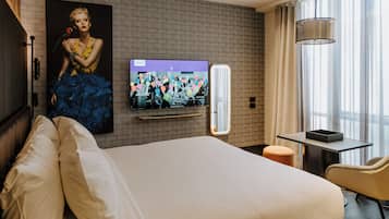 Habitación de hotel con una cama grande, un televisor de pantalla plana montado en la pared, una mesita y una silla.