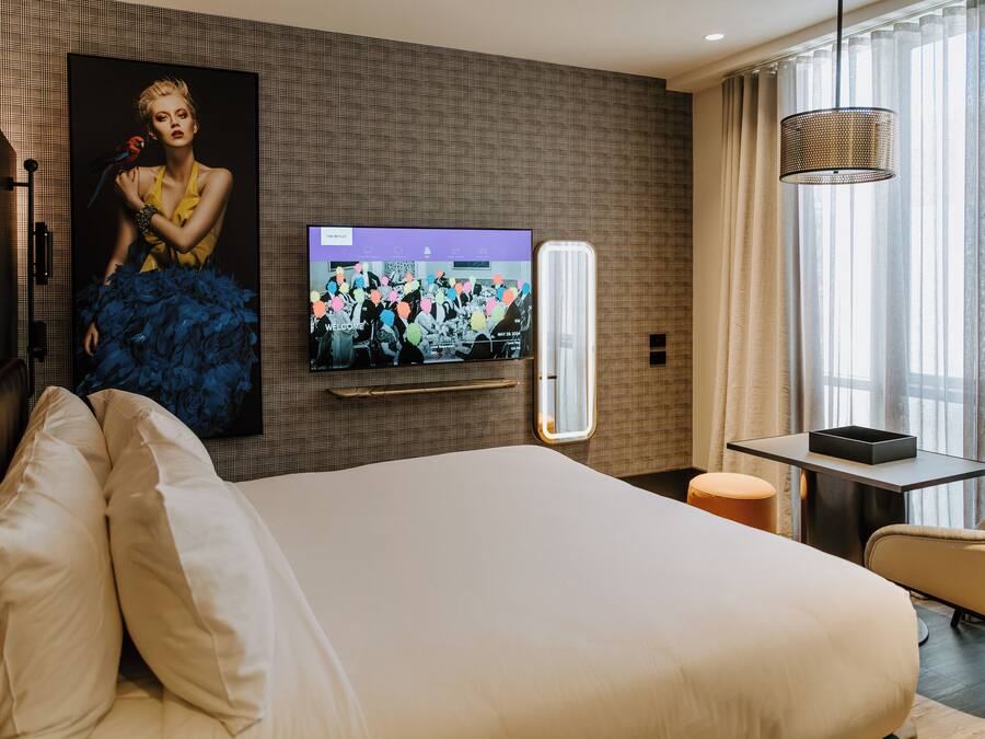 Habitación de hotel con una cama grande, un televisor de pantalla plana montado en la pared, una mesita y una silla.