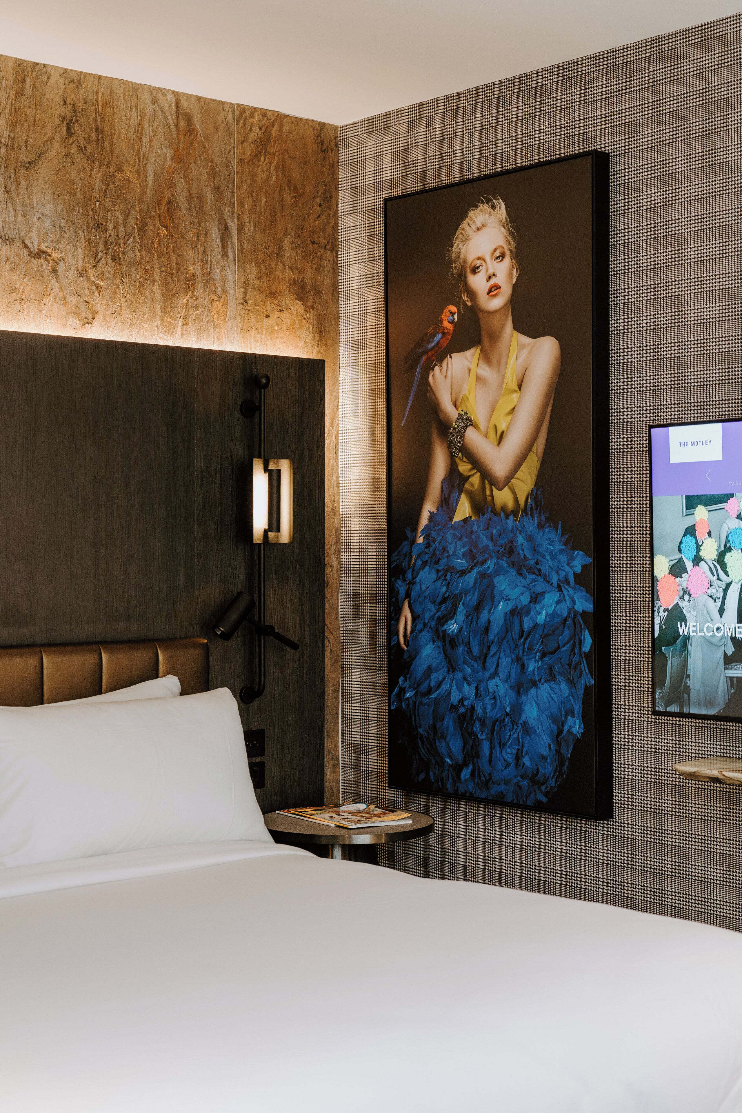 Una habitación de hotel moderna con una cama grande, un televisor montado en la pared y un retrato enmarcado de una mujer con un loro.